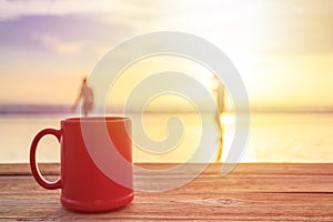 Red coffee cup on wood table at sunset or sunrise beach