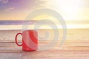 Red coffee cup on wood table at sunset or sunrise beach