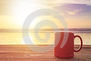 Red coffee cup on wood table at sunset or sunrise beach