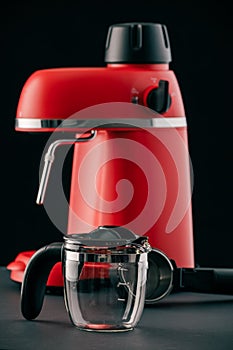 A red coffee machine with chrome parts and a glass pitcher and portafilter against a dark background. Still-life with kitchen