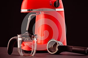 A red coffee machine with a glass pitcher against a black background. Still-life with kitchen utensils for making espresso
