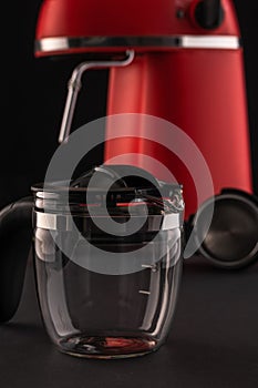 A red coffee machine with a glass pitcher and portafilter against a dark background. Still-life with kitchen utensils for making
