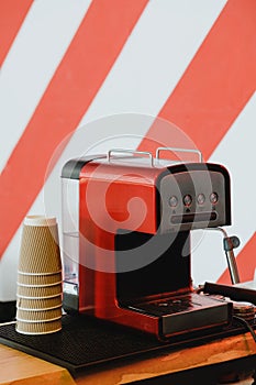 Red coffee machine and paper cups on stripy background wall.