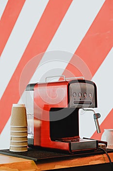 Red coffee machine and paper cups on stripy background wall.