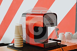 Red coffee machine and paper cups on stripy background wall.