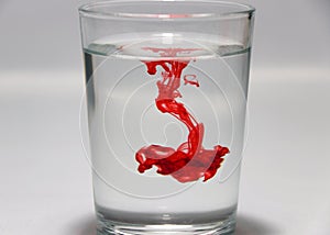 Red color drop on the water in the glass with white background.