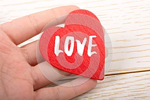 Red color heart shaped object in hand with LOVE wording