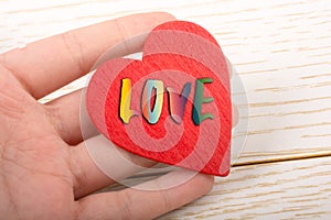 Red color heart shaped object in hand with LOVE wording