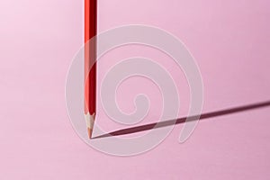 Red color pencil stands on pink paper background.