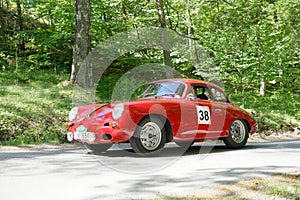 Red color Porche 356 B Karmann Coupe classic car from 1961 driving on a country road