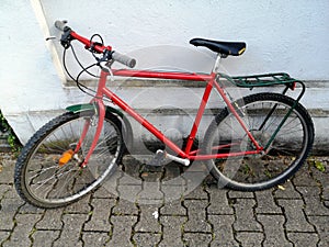 Red colored bicycle leaned on a white wall of a building with old brick flooring