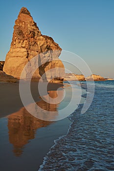 Red colored limestone rock reflecting in the low tide water. Praia do Amado in Algarve, Portugal