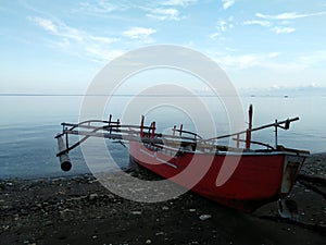 A red colored of traditional fishing canoe on black sandy beach early in the morning