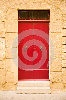 Red colored wooden door, sand stone wall in Medina city, Malta