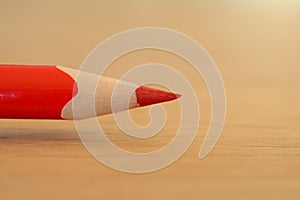 Red coloured pencil on wooden table closeup.