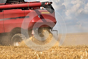 A red combine harvester mows a field of grain. Sunny hot day, ripples of air from the heat, blue sky with clouds. Close-up on the