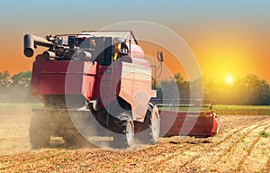 Red combine harvester soybean harvest against the backdrop of the sun in the sky. The farm operates in the field in the autumn sea