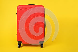 Red comfortable roomy suitcase on wheels with handle for travel stands on yellow background, front view, copy space for