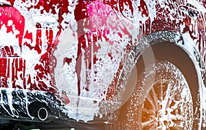 Red compact SUV car with sport and modern design washing with soap. Car covered with white foam. Car care service business concept