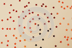 Red confetti in the shape of a star on beige paper background. Festive holiday backdrop. Birthday congratulations Christmas