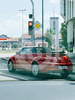 Red convertible car driving in city with VW beetle sign