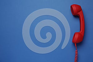 Red corded telephone handset on blue background  top view. Hotline concept