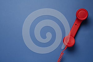 Red corded telephone handset on blue background  top view. Hotline concept