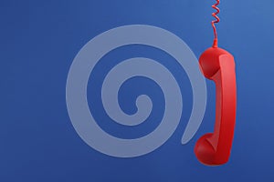 Red corded telephone handset hanging on blue background, space for text. Hotline concept