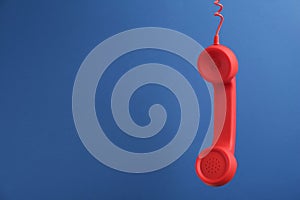 Red corded telephone handset hanging on blue background, space for text. Hotline concept