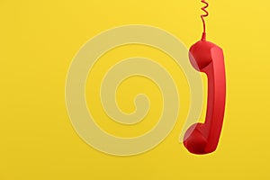 Red corded telephone handset hanging on yellow background, space for text. Hotline concept