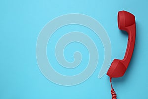 Red corded telephone handset on light blue background  top view. Hotline concept