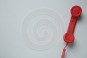 Red corded telephone handset on light grey background, top view. Hotline concept