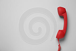 Red corded telephone handset on light grey background, top view. Hotline concept