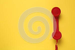 Red corded telephone handset on yellow background  top view. Hotline concept