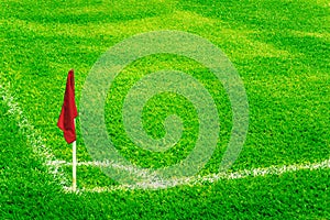 Red corner flag on a football field with bright fresh green turf grass and white soccer touch lines.