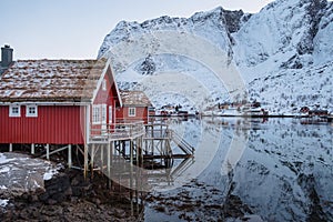 Red cottage on coastline in fishing village with snow mountain at Lofoten Islands