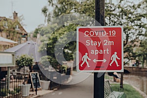 Red Covid-19 Stay 2 Metres Apart sign on a sidewalk in Bourton-on-Water, Cotswolds, UK