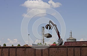 Red crane throwing metal industrial waste into a train container at railway station |chimney