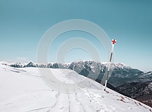 Red cross hiking trail mark on a pole with huge mountain in the background. Winter landscape in Bucegi Mountains Romania