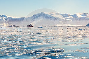 Red cruise steamboat drifting afar among the icebergs with huge rock and glacier in background, Neco bay, Antarctica