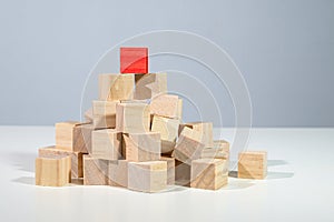 Red cube on the top of a heap from light wooden cubes, concept for business, career, and success, gray background with copy space