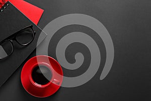 Red cup with aromatic coffee, notepads and glasses on black background, flat lay. Space for text