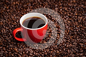 Red Cup of black coffee on table covered with coffee beans
