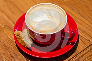 Red cup with cappuccino coffee with lush foam and heart on wooden background. meeting on valentines day.