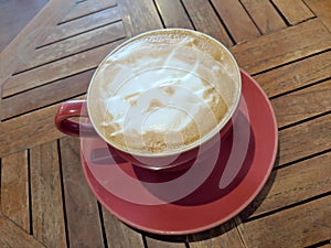 Red cup of Cappuccino on saucer with a cat face pattern in foam