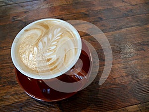 Red cup of Cappuccino on saucer with a leaf pattern