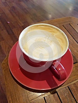 Red cup of Cappuccino on saucer with a leaf pattern in foam