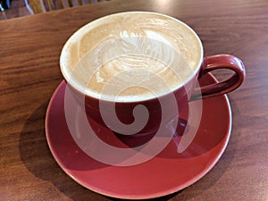 Red cup of Cappuccino on saucer with a leaf pattern in foam