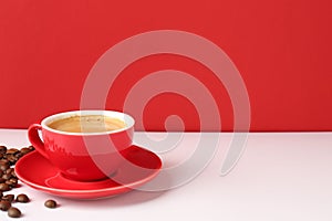 Red cup with coffee and roasted beans on white table, space for text