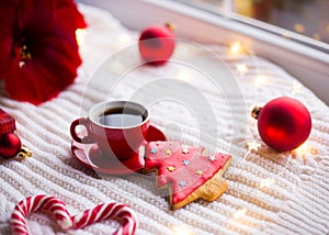 Red cup with espresso coffee and gingerbread in form of fir on white knitted plaid surrounded with winter decor.